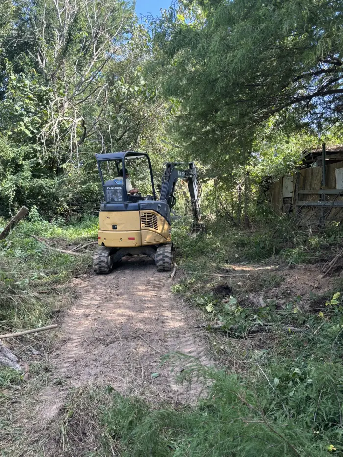 An excavator working a narrow path cut through dense woodland