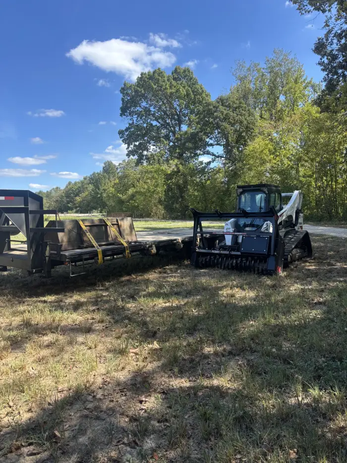 A track loader parked beside an equipment trailer at a property