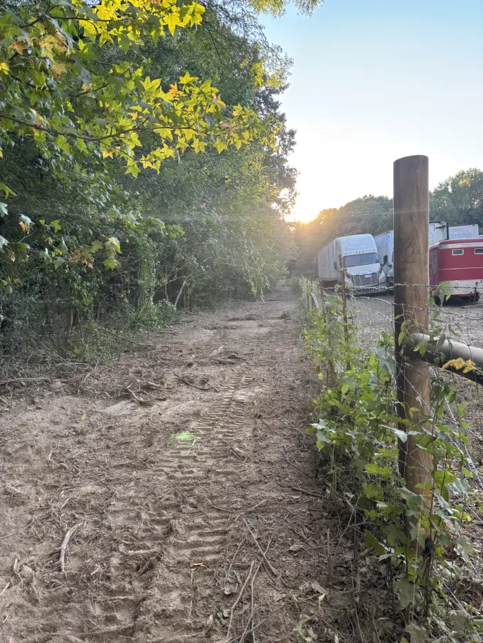 A freshly cleared track running along a fence line toward a low evening sun